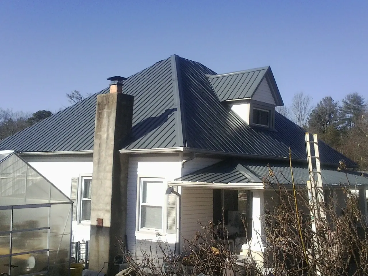 Dark blue standing seam metal roof on a white farmhouse with dormer — Slate & Tile Roof Repair by Roofing Brothers in Holly Bluff