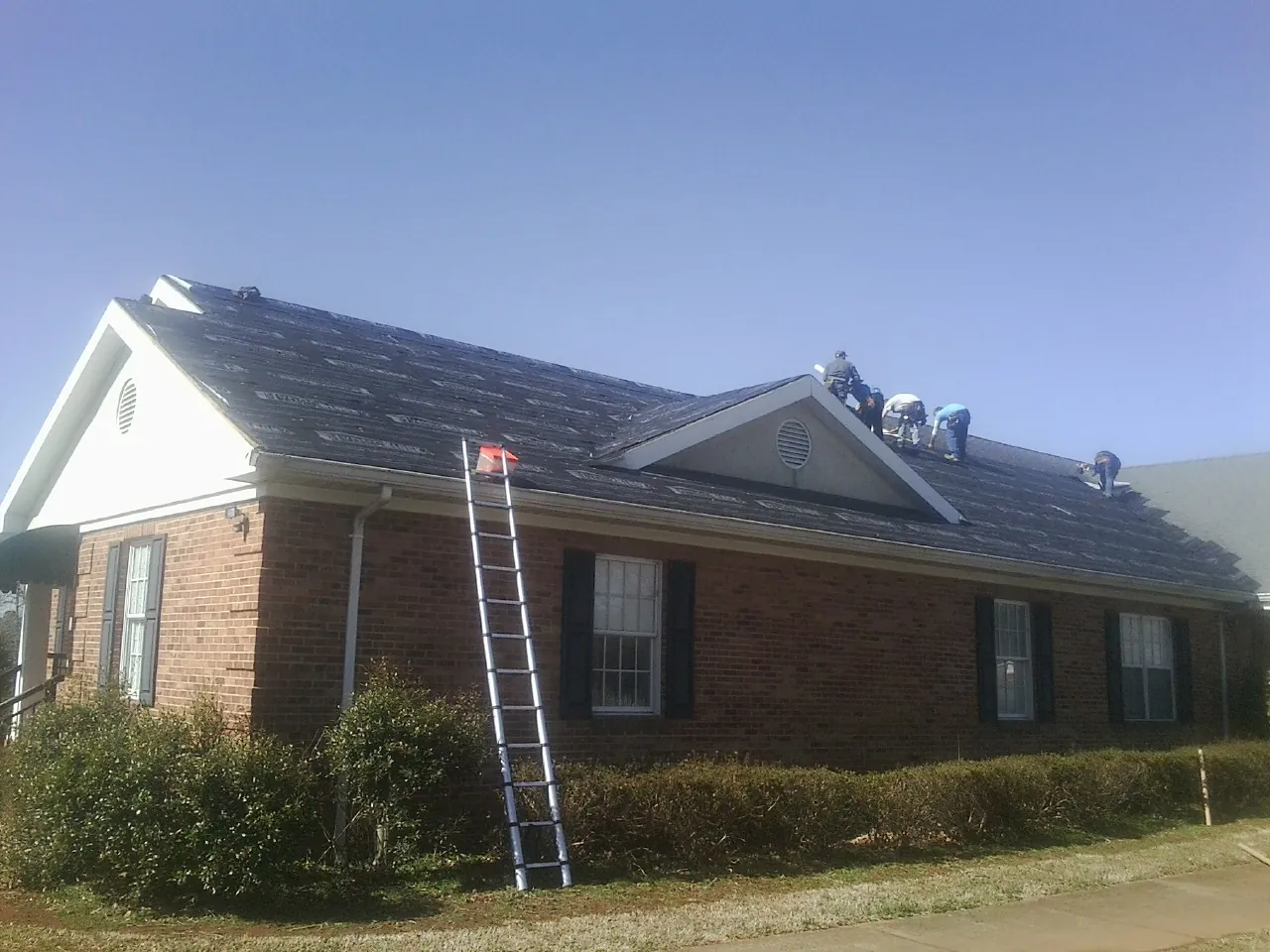 Crew tearing shingles off a brick ranch roof with a ladder set — Emergency Roof Repair work by our crew in Holly Bluff