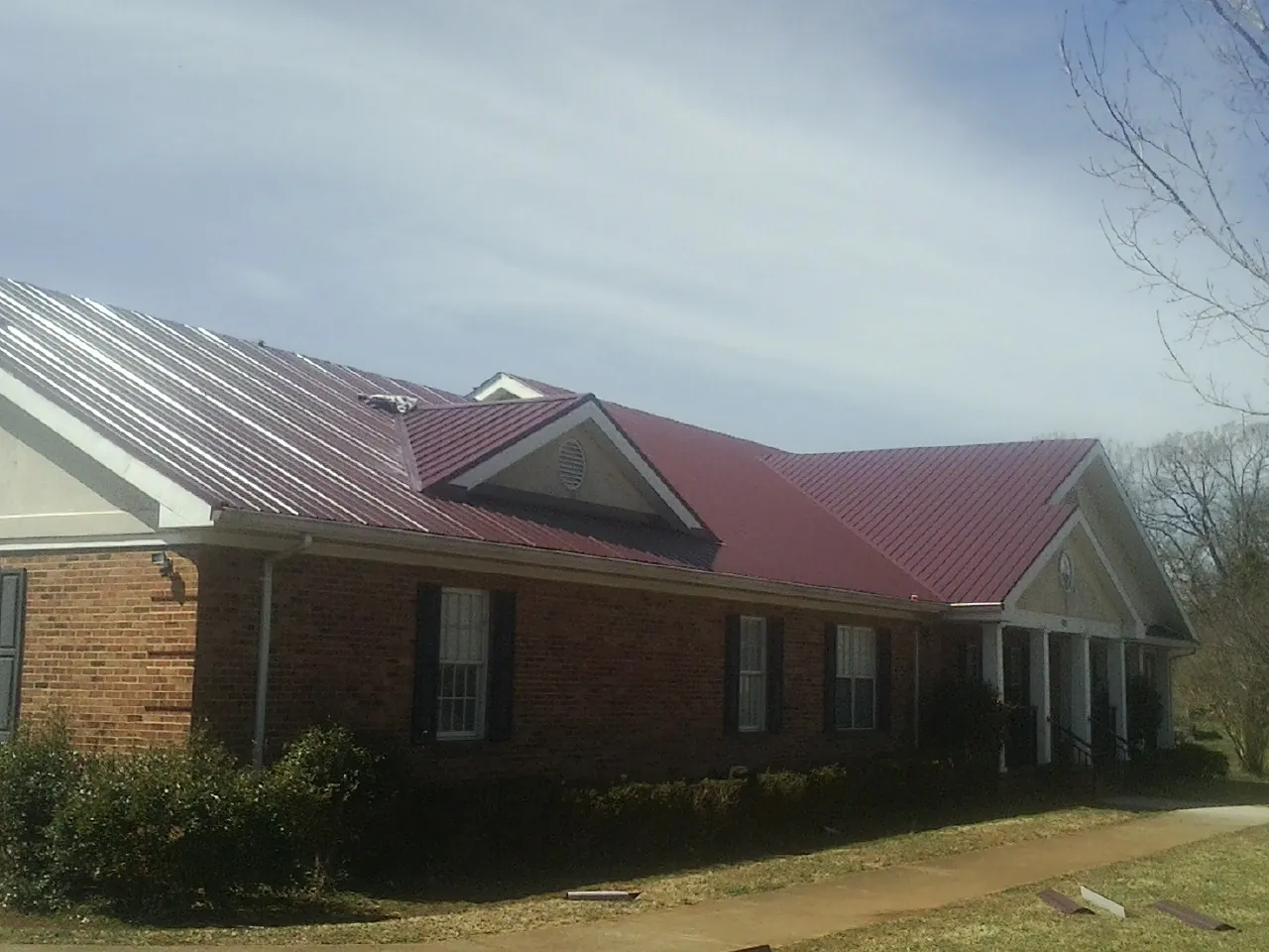 Red metal roof with gabled entries on a long brick building, from a Hail Damage Roof Repair job in Holly Bluff