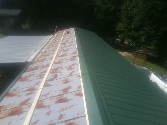 Old rusted panels beside newly installed green metal roofing — Wind Damage Roof Repair by Roofing Brothers in Holly Bluff