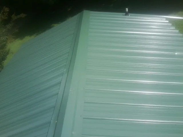 New green metal panels meeting at the ridge of a roof — Flat Roof Repair work by our crew in Holly Bluff