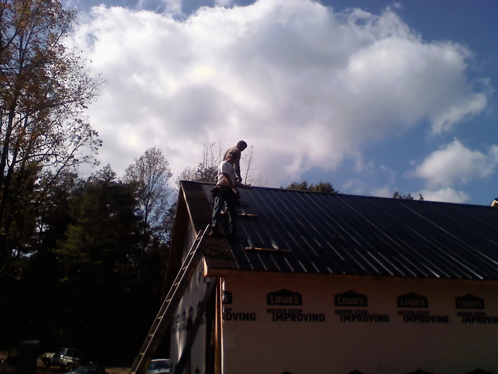 Roofer fastening dark metal panels high against a cloudy sky, from a Roof Inspection job in Holly Bluff