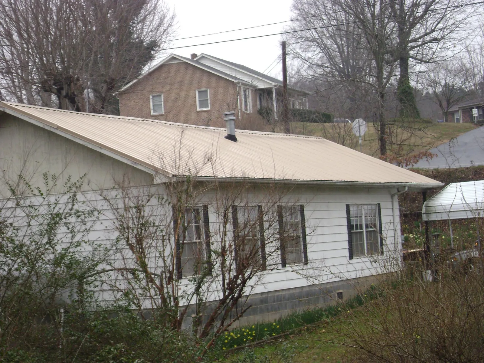 Tan metal roof on a white sided house set into a hillside — Commercial Roofing by Roofing Brothers in Holly Bluff