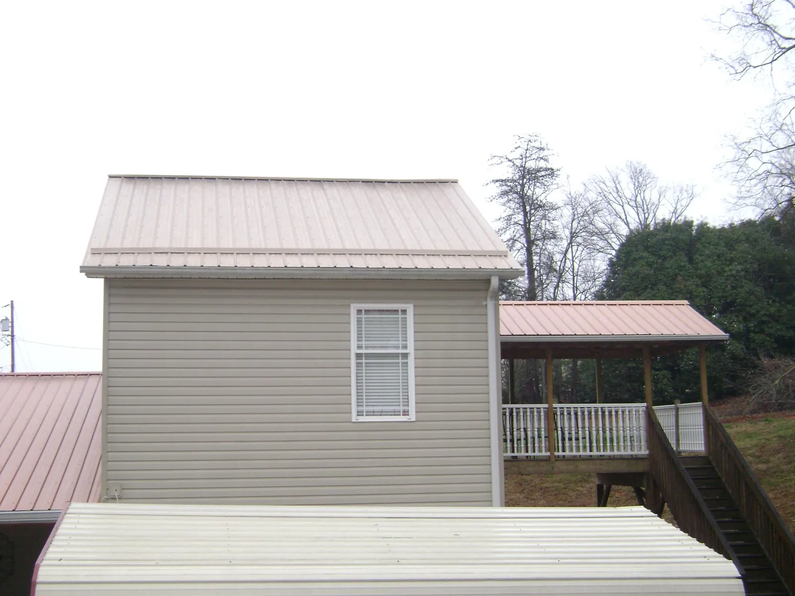 Tan metal roofs on a two story addition and attached porch, from a Roof Replacement job in Holly Bluff